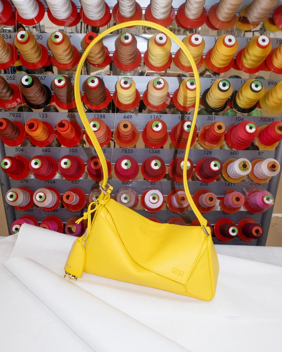Loewe making of: a yellow bag in the workshop in front of a wall of thread spools