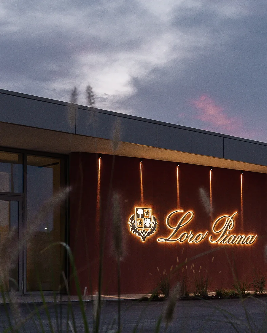 Facade of the Loro Piana knitwear manufacture in Ghemme at dusk, with the illuminated Loro Piana lettering